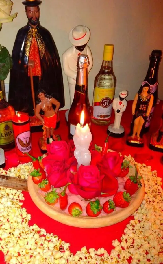 Altar vermelho com rosas, morangos, pimentas e uma vela acesa, cercado de pipoca e das imagens das entidades